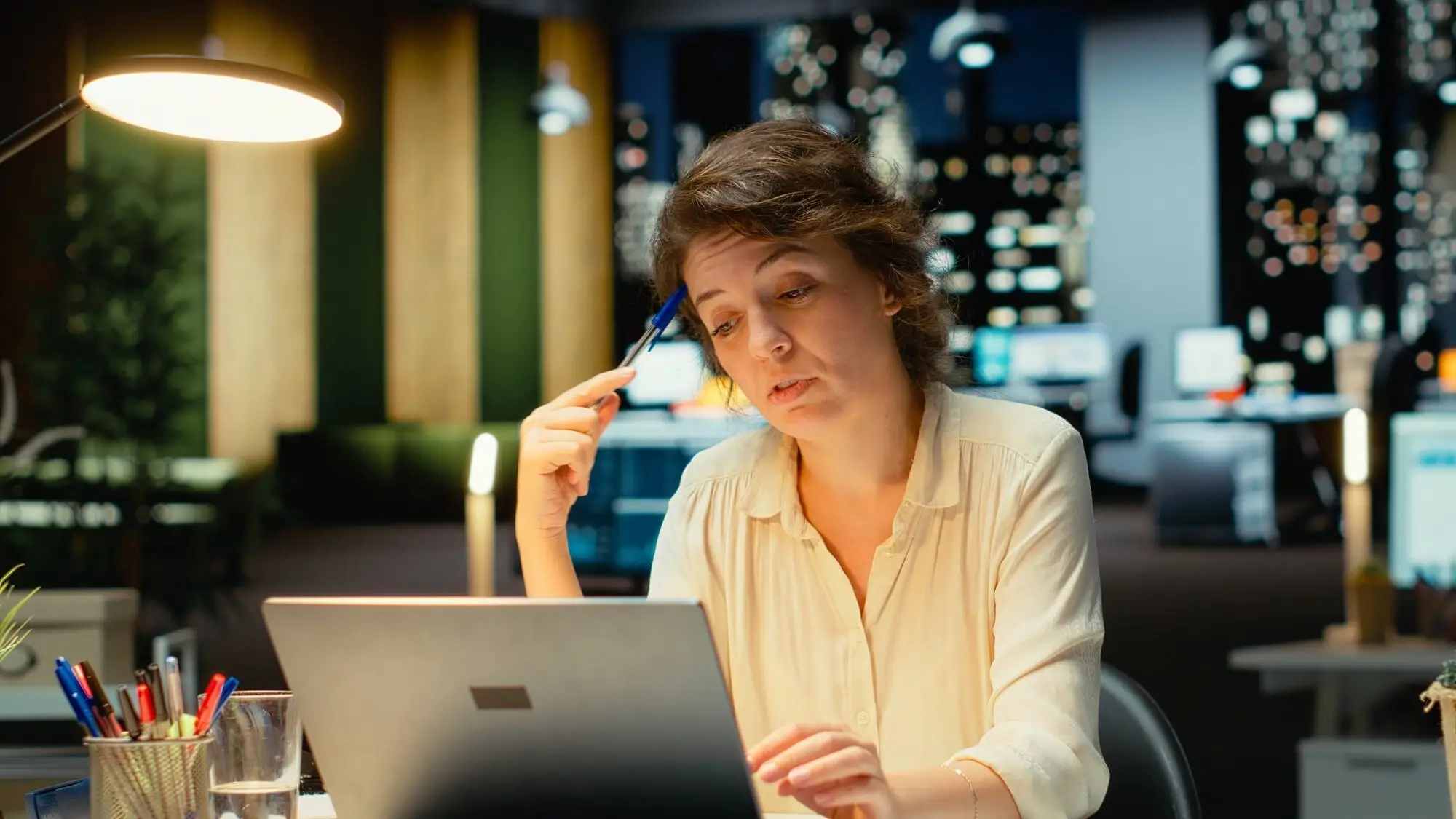 Frau sitzt abends im Büro nachdenklich vor ihrem Laptop