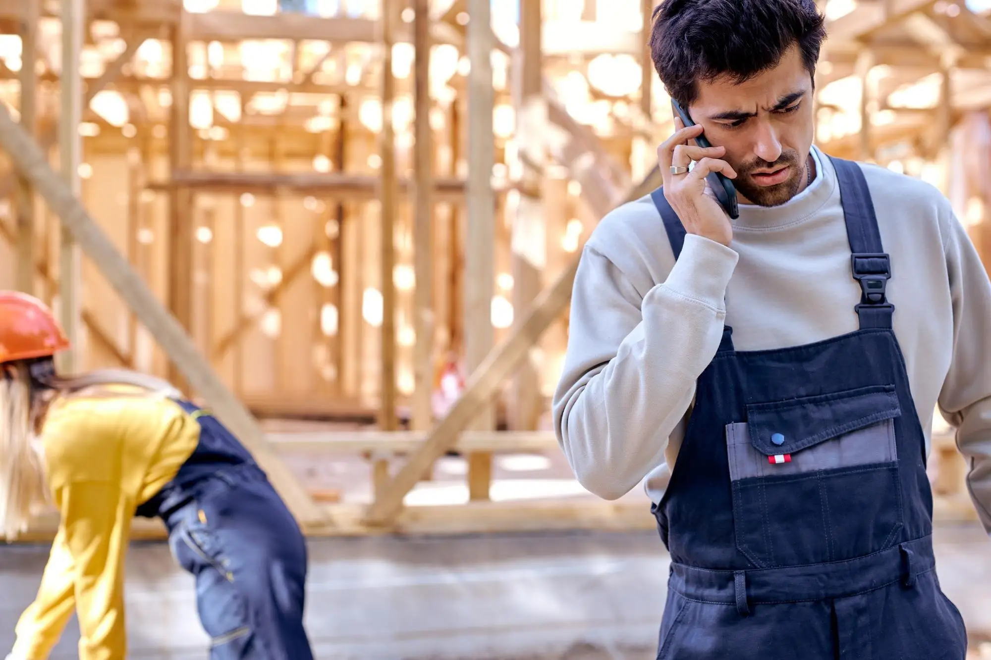 Handwerker in Arbeitslatzhose telefoniert auf einer Baustelle