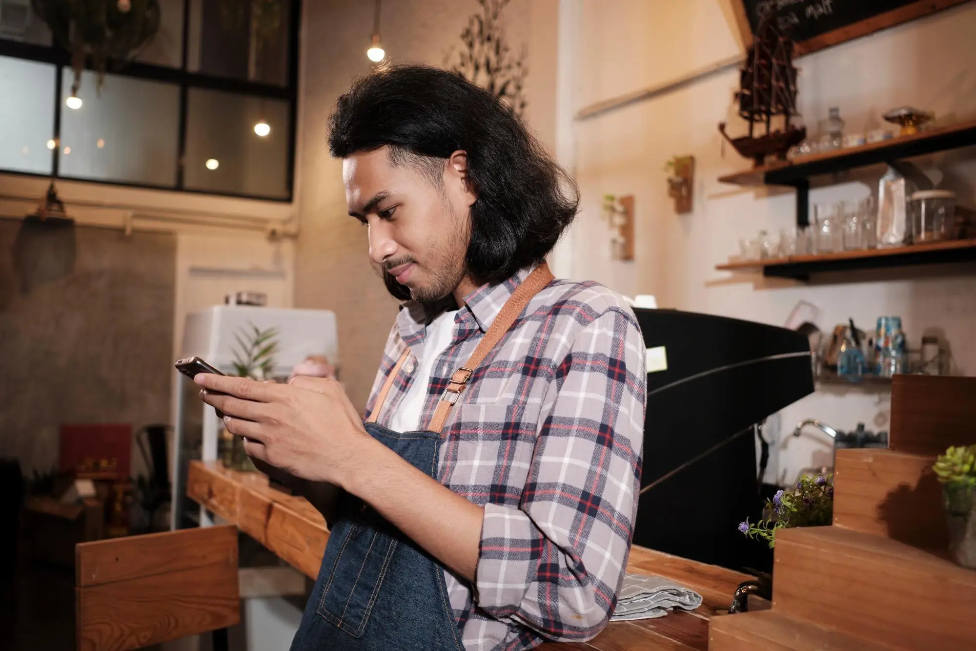 Inhaber eines Cafés schaut stirnrunzelnd auf sein Smartphone