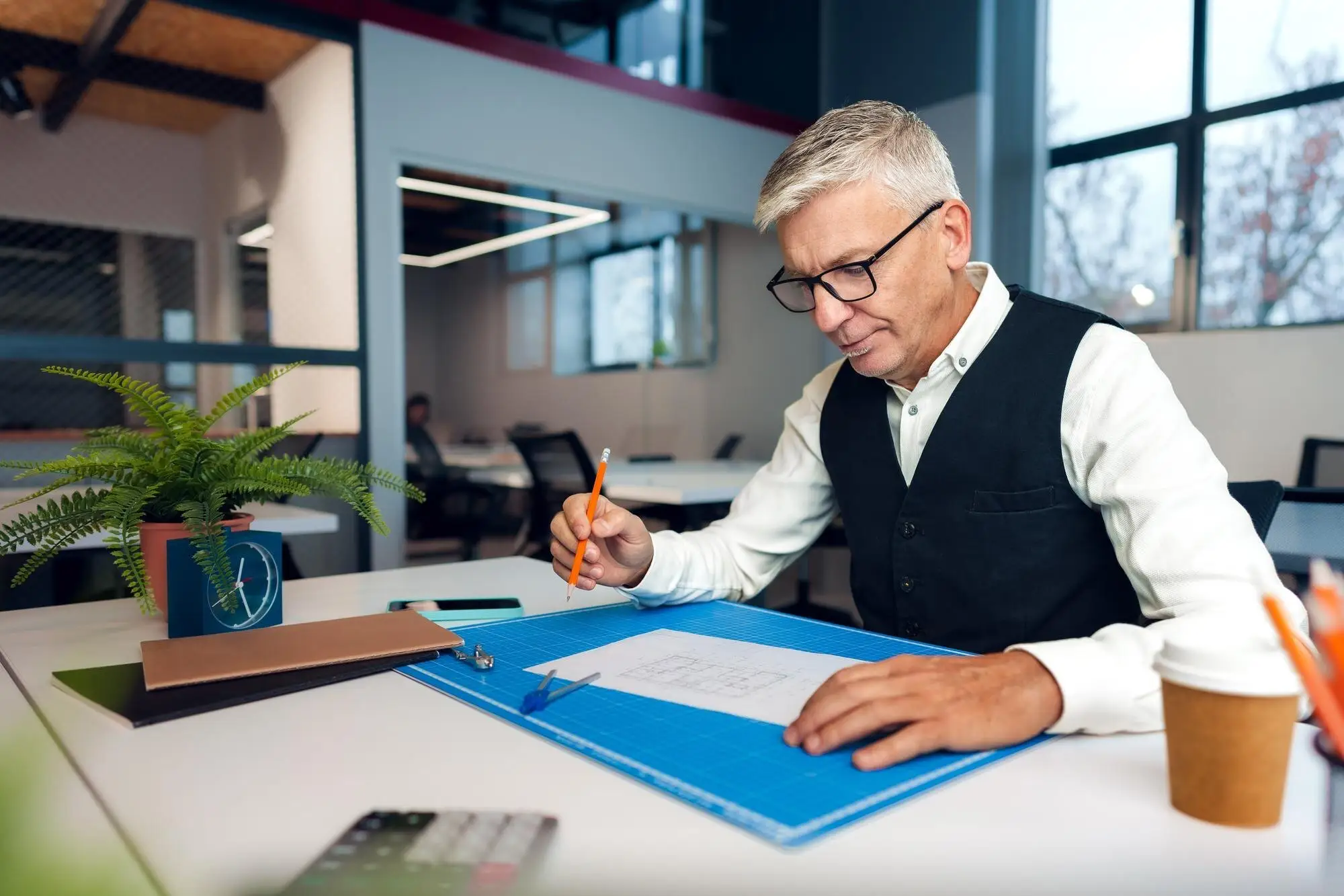 Inhaber mit Brille geht an seinem Schreibtisch Unterlagen durch