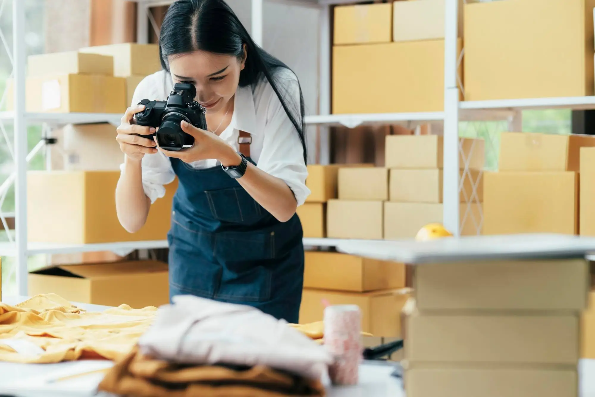 Frau fotografiert Produkte in einem Lager voller Kartons