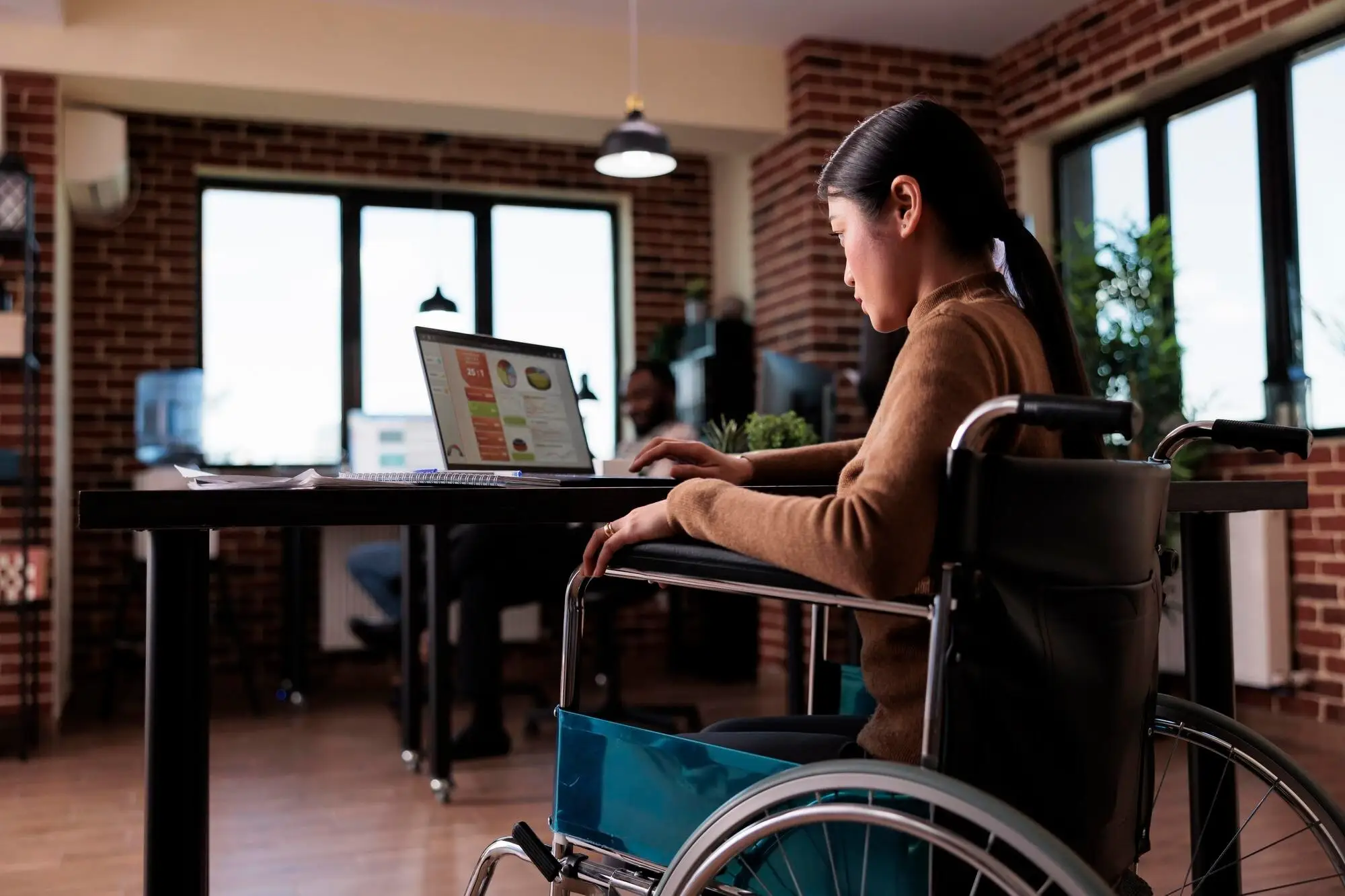 Frau im Rollstuhl arbeitet in einem Büro am Laptop