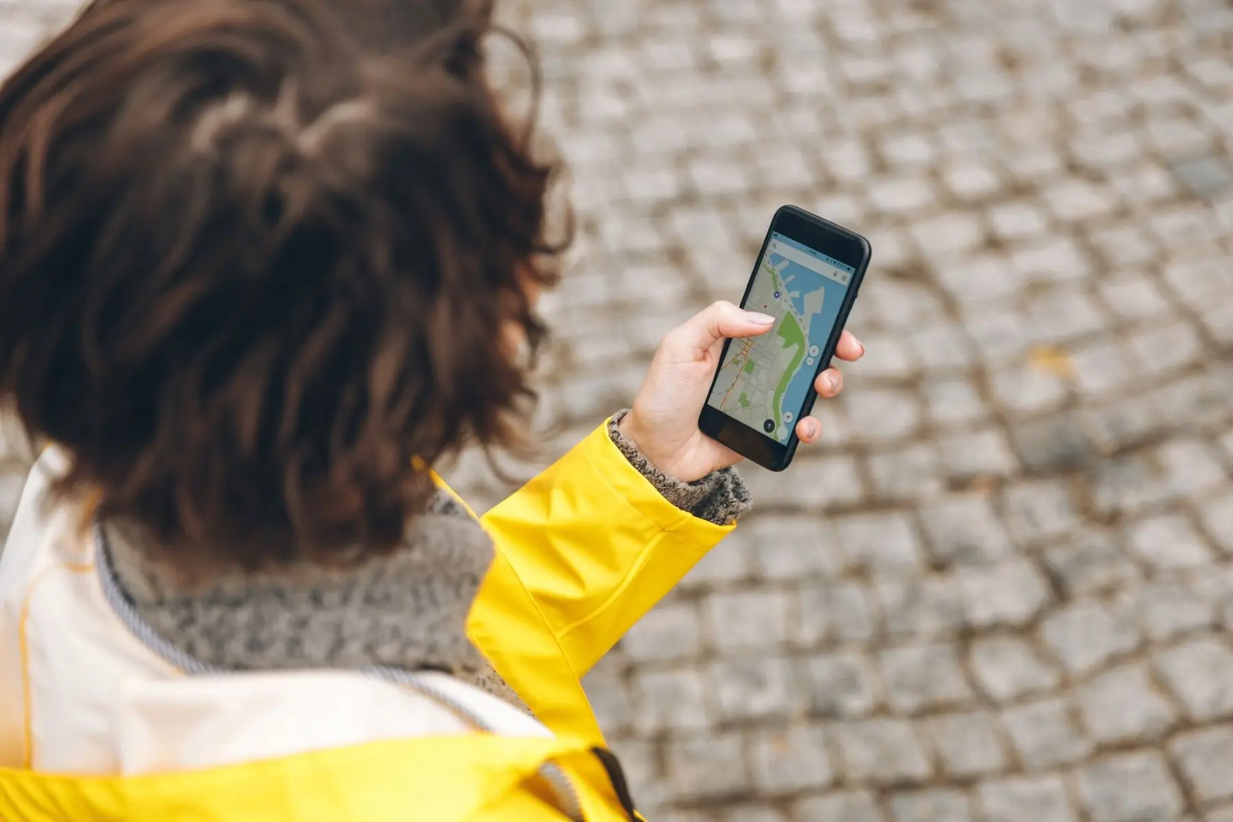 Eine Person sucht auf dem Smartphone einen Ort auf der Karte, im Hintergrund Kopfsteinpflaster