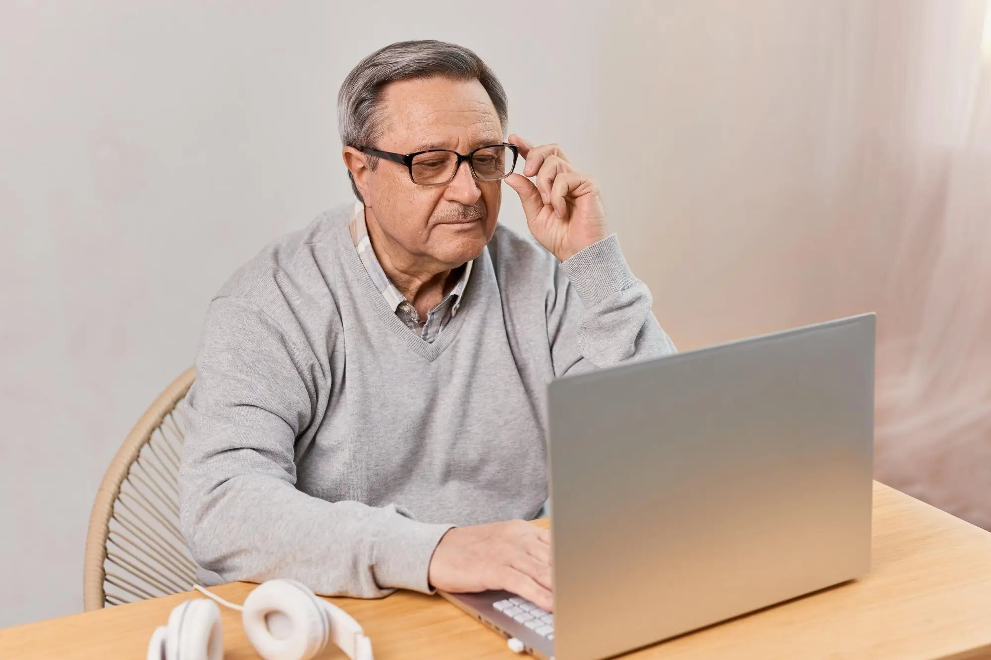 Älterer Mann rückt seine Brille zurecht und schaut auf den Laptop