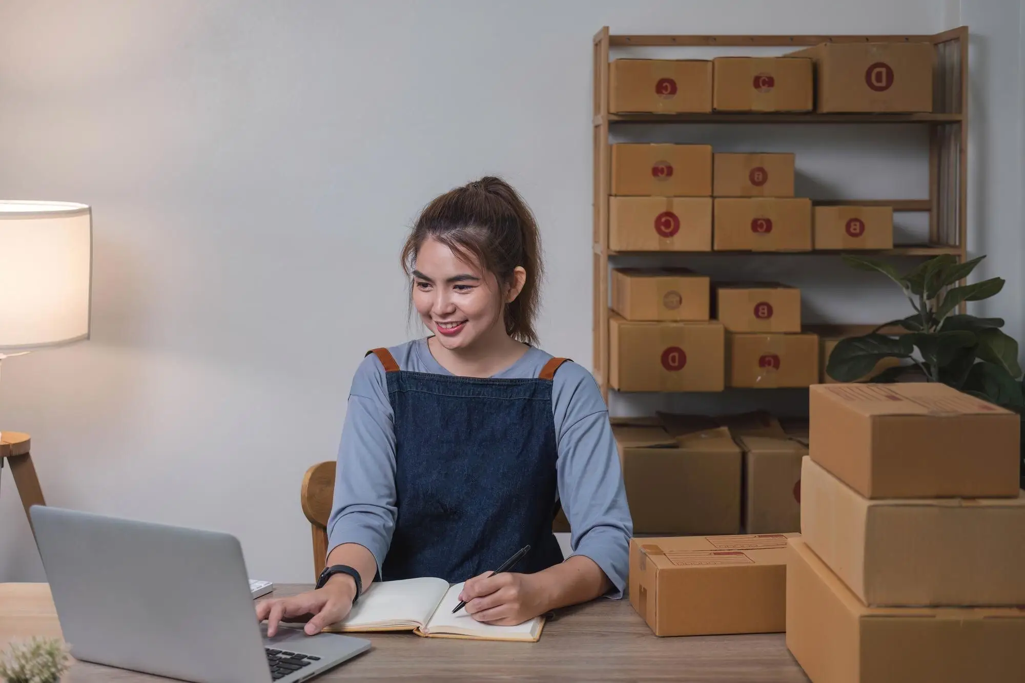 Inhaberin eines kleinen Versandhandels arbeitet am Laptop zwischen Kartons
