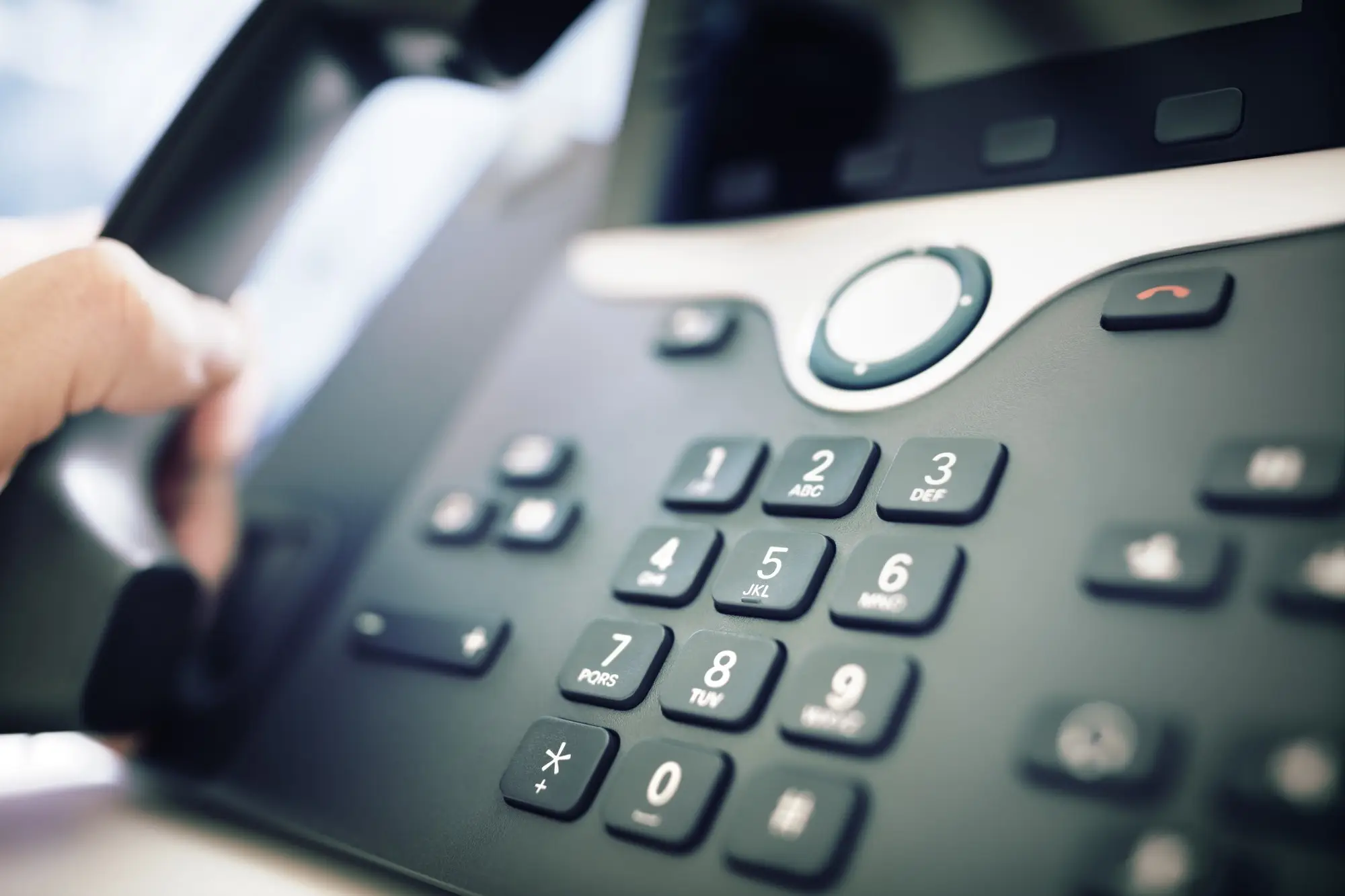 Eine Hand drückt eine Taste auf dem Keypad eines Bürotelefons