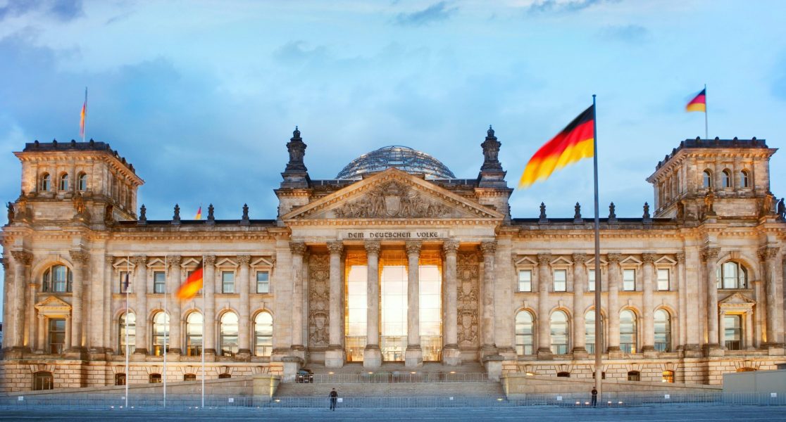 german – 6 Beleuchteter Reichstag in Berlin bei Abendlicht, mit wehenden deutschen Flaggen.