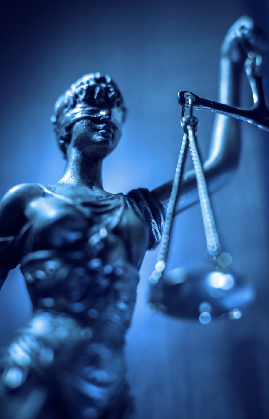 lady justice statue with scales and blindfold Statue der Justitia mit Augenbinde und Waage vor blauem Hintergrund.